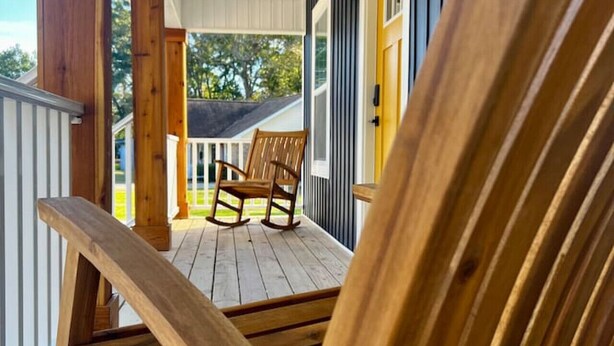A wooden rocking chair on a porch with a view of a house and trees. - Quiet 2 Bedroom home near the Beach! (Sunset Beach)