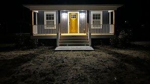 A two-story house with a yellow front door, white railings, and a number '8970' on the steps. - Quiet 2 Bedroom home near the Beach! (Sunset Beach)