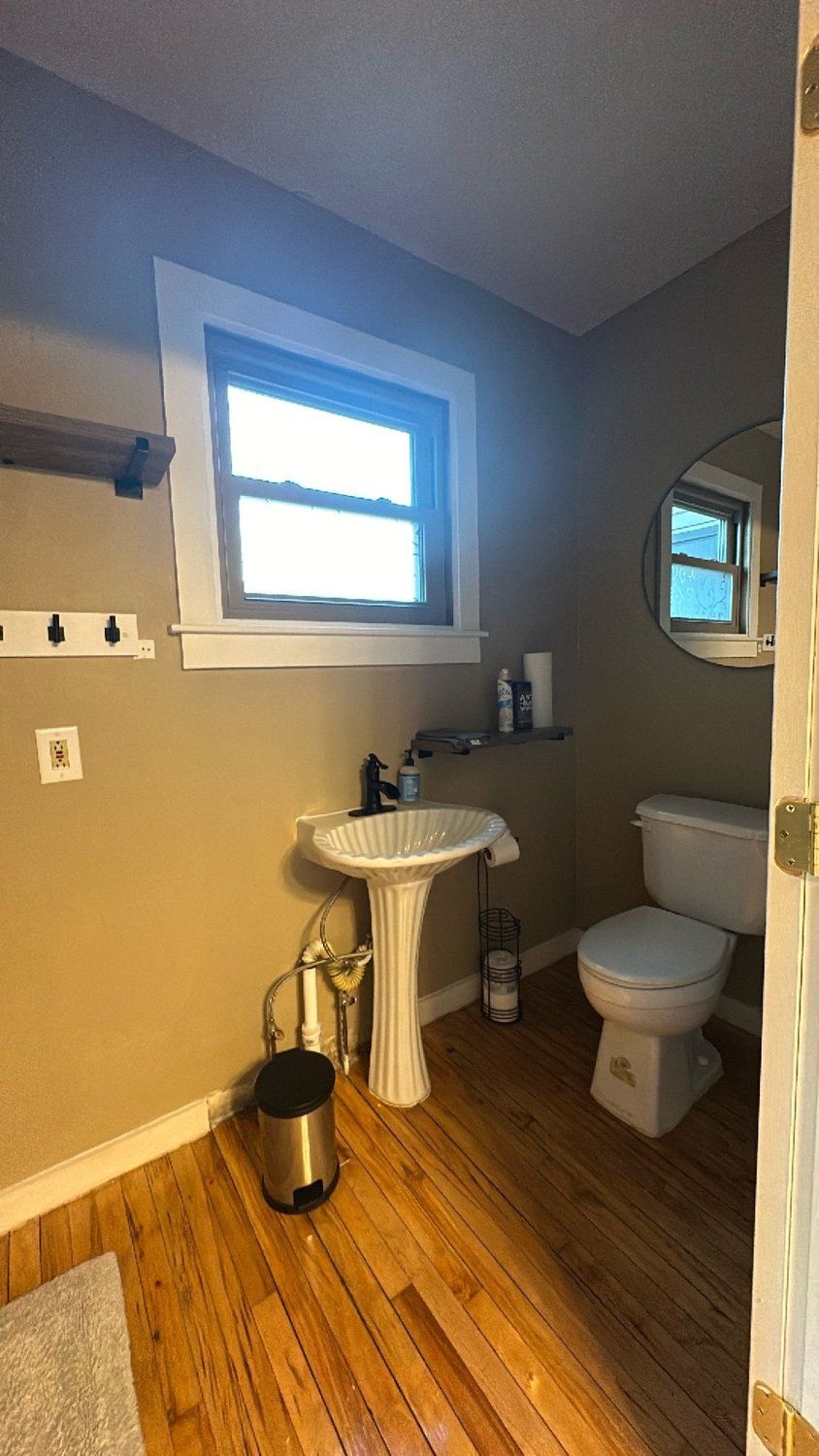 A bathroom with a pedestal sink, a toilet, a window, and a mirror.