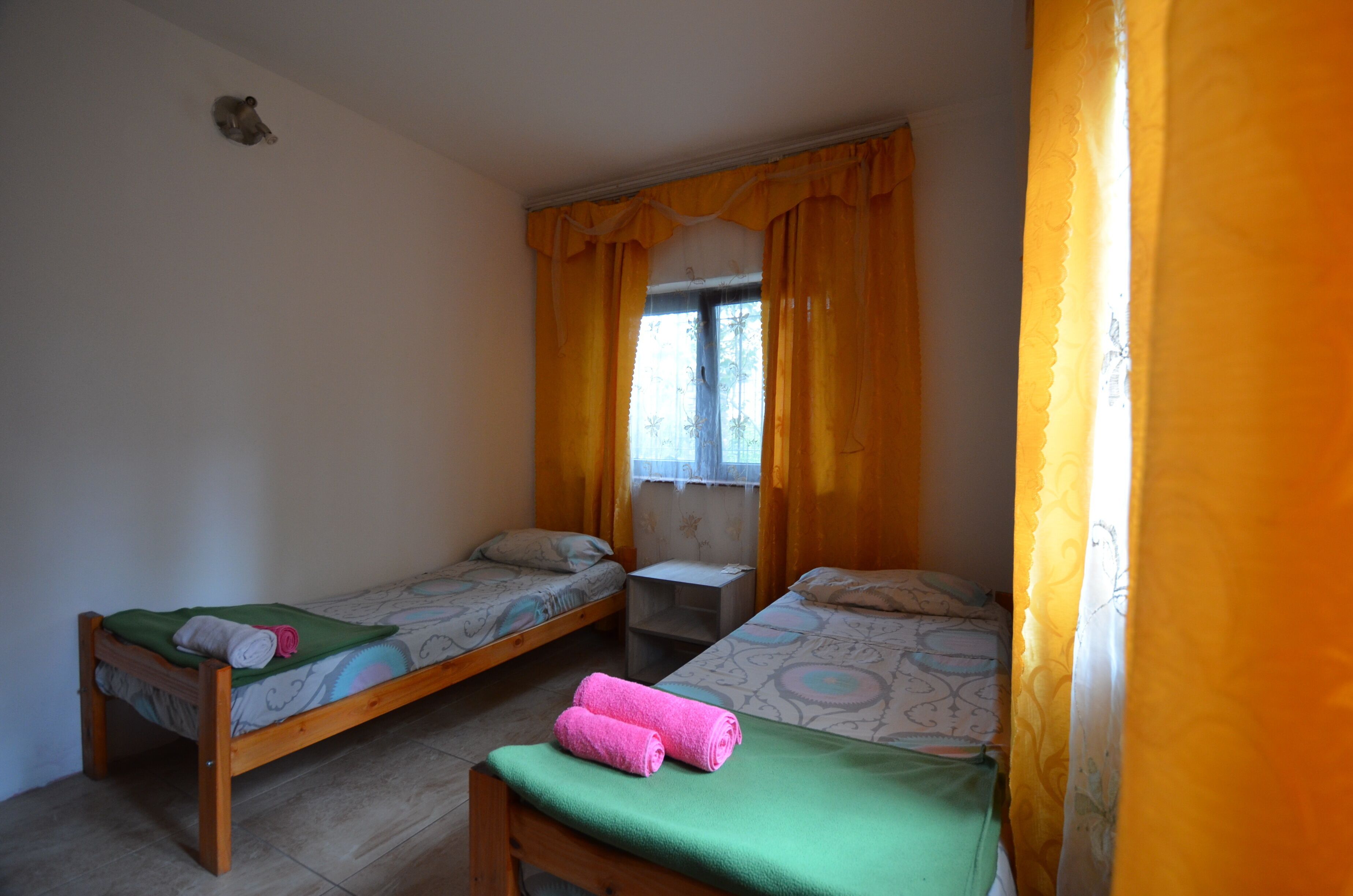 A small, simple room with two single beds, a small table, and a window with curtains.