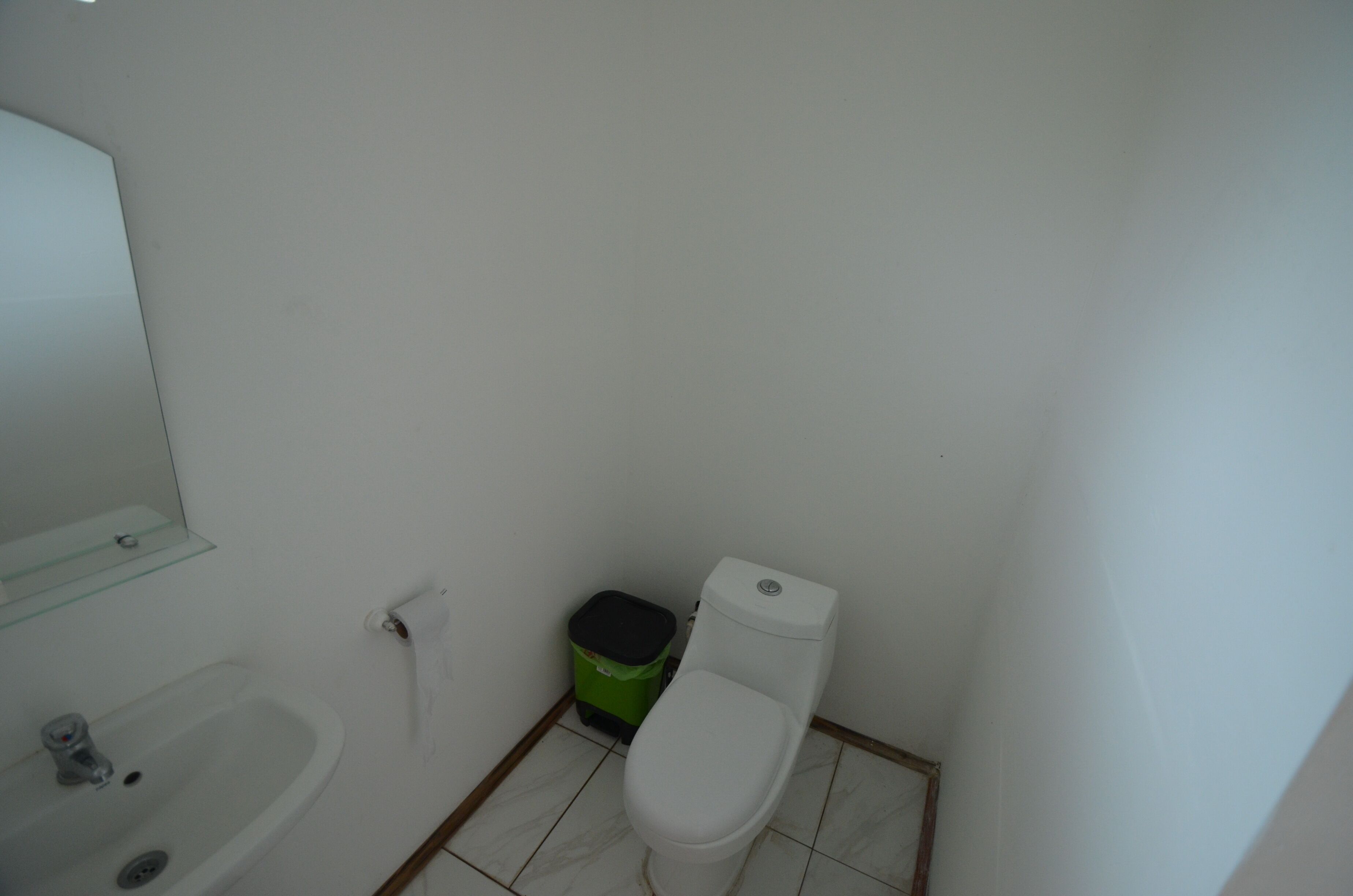 A small bathroom with a white sink, toilet, and green trash bin.