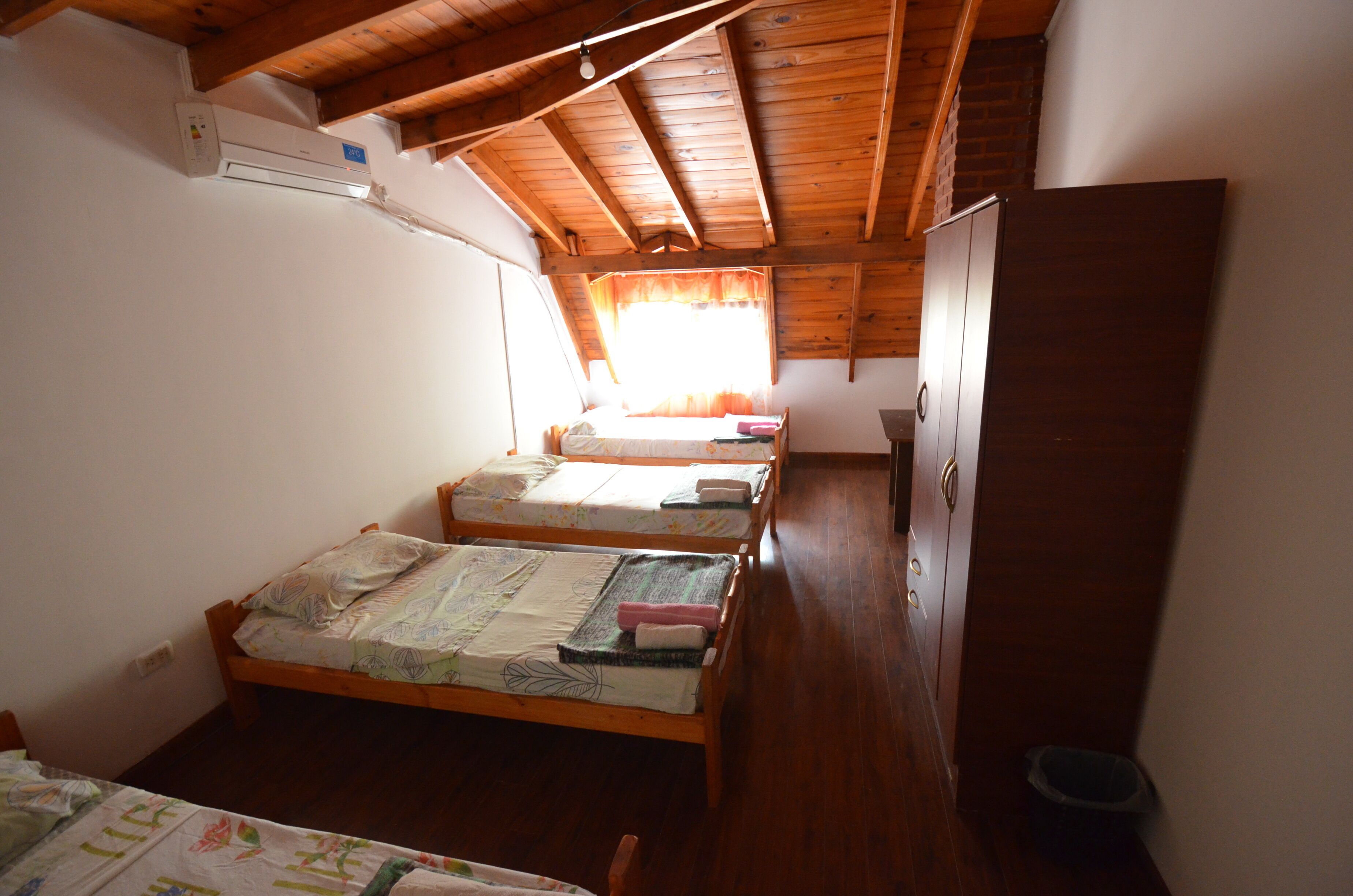 A small, single-room accommodation with two wooden bunk beds, a wooden ceiling, and a window with curtains.