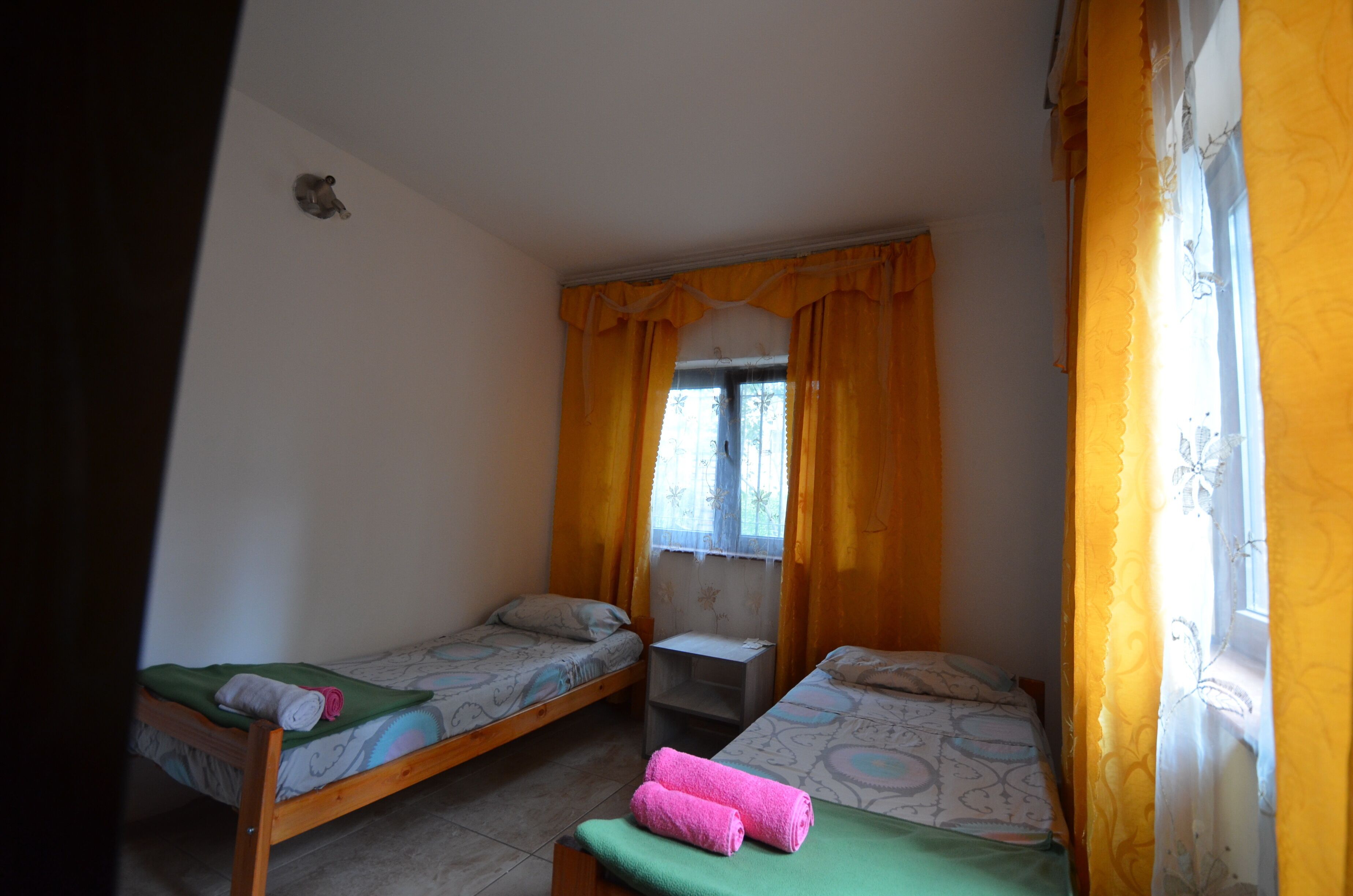 A small room with two single beds, a window with curtains, and a small table.