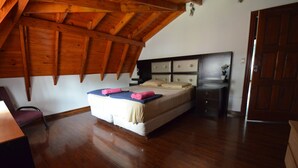 Een slaapkamer met een houten plafond, een bed met hoofdeinde, een nachtkastje en een deur.