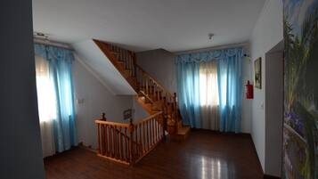 A spacious room with a wooden staircase, a large window with blue curtains, and a painting on the wall.
