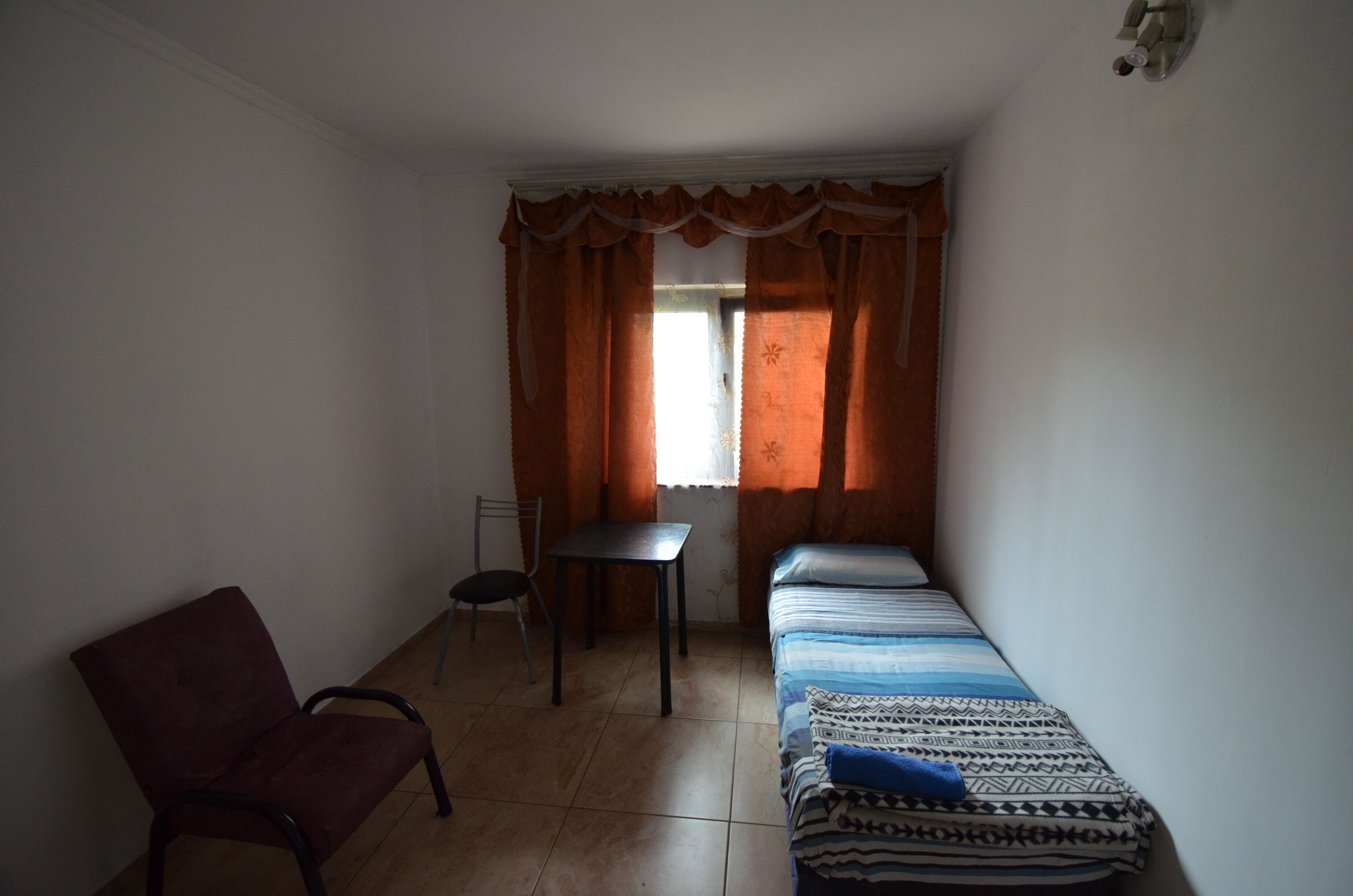 A small, dimly lit room with a single bed, a chair, and a table.