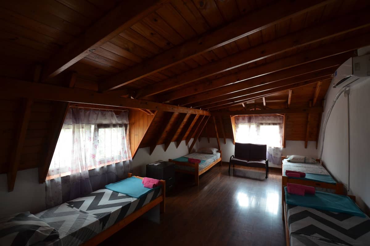 Ein gemütliches Schlafzimmer im Dachgeschoss mit Holzbalken, zwei Einzelbetten, einem Schreibtisch und einem Sessel.