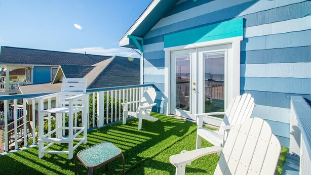 A blue and white house with a balcony, white chairs, and a small table.