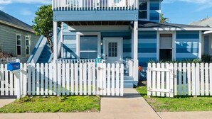 A two-story house with a balcony, a white picket fence, and a clear blue sky.