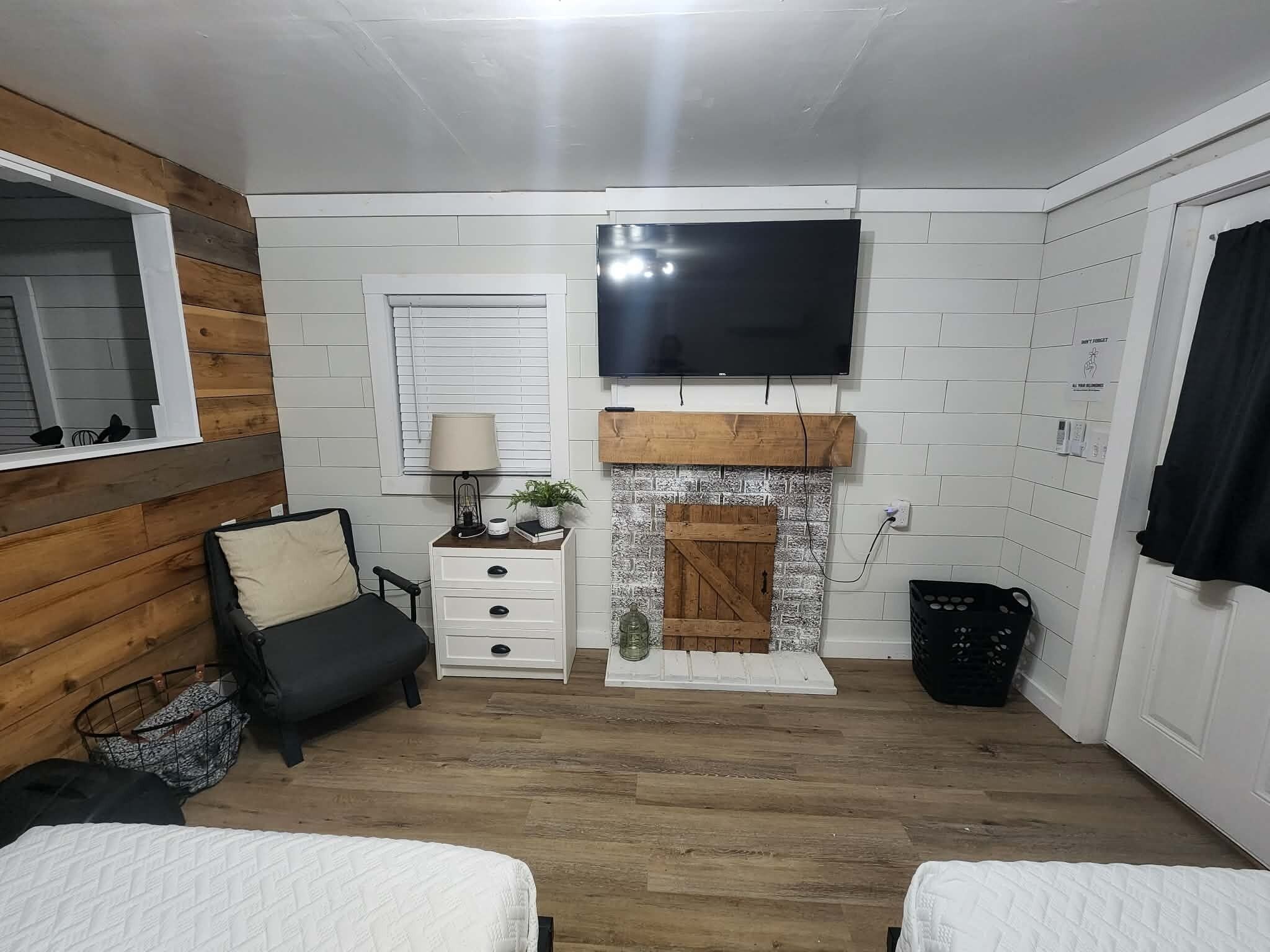 Une pièce avec une cheminée, un téléviseur fixé au mur, un lit, une table de chevet et une fenêtre avec des stores.