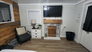 Une pièce avec une cheminée, un téléviseur fixé au mur, un lit, une table de chevet et une fenêtre avec des stores.