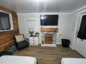 Una habitación con chimenea, televisor montado en la pared, cama, mesita de noche y ventana con persianas.
