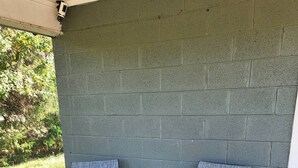 Deux chaises d’extérieur, dotées d’une structure en métal et d’un assise en tissu bleu, sont placées sur une terrasse en béton, adossées à un mur en briques vertes.