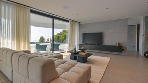 Uma sala de estar moderna com um sofá grande, uma televisão de tela plana e uma mesa de jantar com um jogo de xadrez.