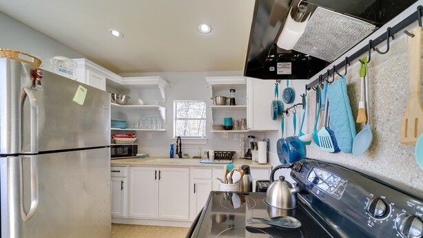 A modern kitchen with white cabinets, a stainless steel refrigerator, a black stove, and various kitchen utensils hanging on the wall. - Cozy Bandera Cottage w/ Medina River Access! (Bandera)