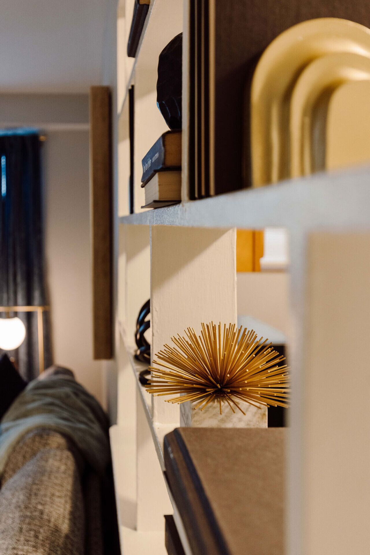 Un interior moderno con una estantería blanca que contiene libros y un objeto dorado decorativo.