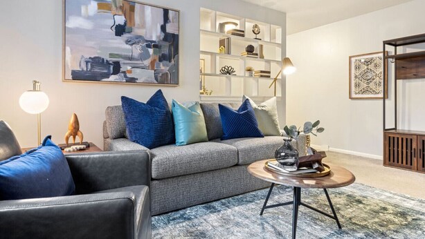 Un salon moderne avec un canapé gris, des coussins bleus, une table basse ronde et une bibliothèque.