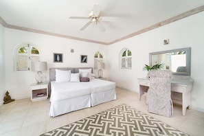 Quarto com cama, mesas de cabeceira, escrivaninha, cadeira, ventilador de teto e espelho.