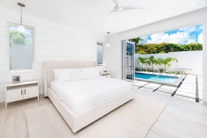 A bedroom with a large bed, a nightstand, a bedside table, a window, and a view of a swimming pool.