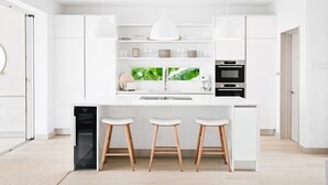 Een moderne keuken met witte kasten, een centraal eiland met krukken, een inbouwoven en een vaatwasser.