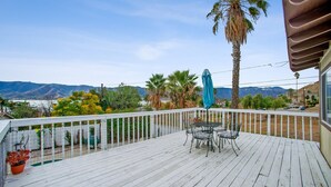 Una terraza de madera con mesa y sillas, con vista a un paisaje montañoso.