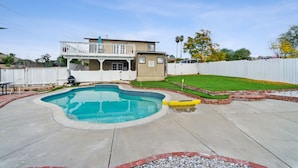 Una propiedad residencial con piscina, patio cercado y una casa de dos pisos con balcón.