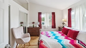 Un dormitorio con cama, una silla, cómoda y ventana con cortinas.