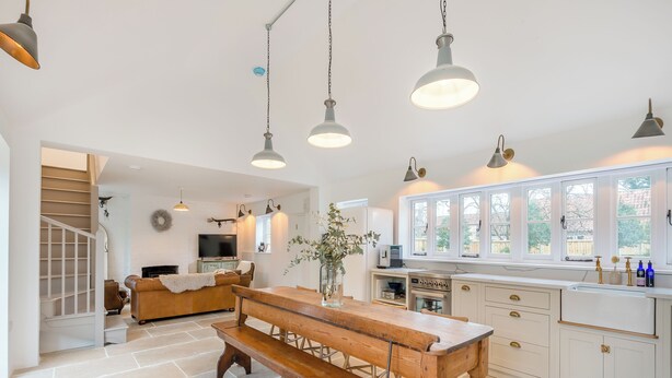 Una cocina amplia con banco de madera, armarios blancos e iluminación colgante.