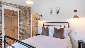 Un dormitorio con una cama, una puerta de madera, una pared de ladrillo y una lámpara colgante.
