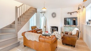 Una sala de estar con escalera, sofás de cuero, chimenea y televisor.