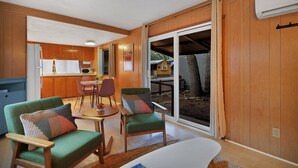 A cozy living area with a dining table, two green armchairs, and a white sofa. A kitchen with wooden cabinets and a refrigerator is visible in the background. - Modern Cabin (Olive) (Dunsmuir)