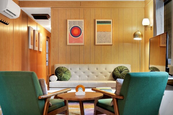 A room with a sofa, two armchairs, a small round table, and two wall-mounted artworks.