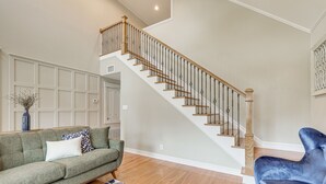 A spacious living room with a wooden staircase, a green sofa, a blue armchair, and a patterned rug. - Brenham Rental w/ Deck & Yard < 1 Mi to Downtown! (Brenham)