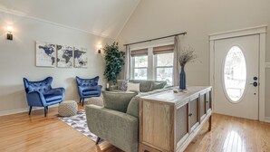 A living room with a high ceiling, wooden flooring, two blue armchairs, a green sofa, a wooden coffee table, and a world map artwork on the wall. - Brenham Rental w/ Deck & Yard < 1 Mi to Downtown! (Brenham)