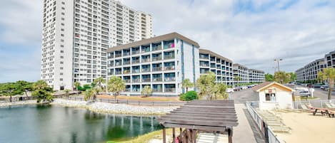 A multi-story hotel with balconies, a pool, and a small beach area with a gazebo.