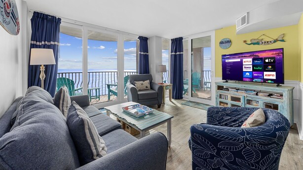 Una sala de estar con sofá, sillón y mesa de centro, televisor sobre un mueble bajo y balcón con vistas.