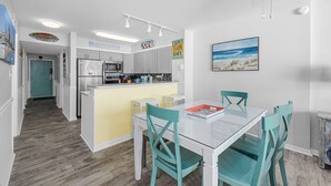 Una cocina moderna con armarios blancos, una isla amarilla y un comedor con mesa de vidrio y sillas turquesas.