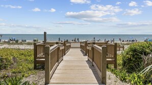 Un muelle de madera que lleva a una playa con gente y sombrillas.