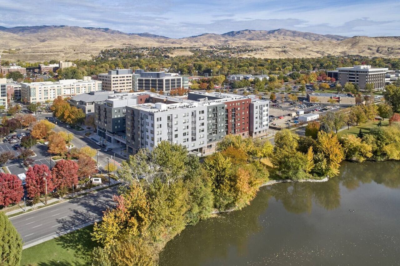A multi-story building with a modern architectural design, surrounded by a mix of deciduous trees and a body of water.