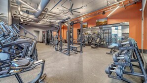 Un gimnasio con diversos equipos de ejercicio, incluyendo cintas de correr y máquinas de pesas, con paredes naranja y un techo con tuberías a la vista.
