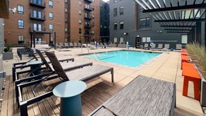 Un área de piscina en la azotea con sillones y una mesa, rodeada de edificios modernos.