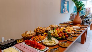 Een buffet met diverse etenswaren, zoals fruit, gebak en vlees, op een houten tafel in een goed verlichte ruimte.
