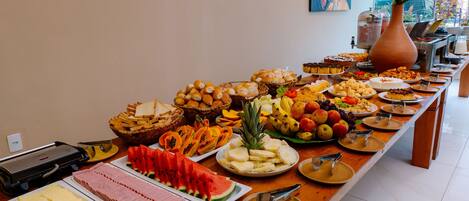 A buffet table with various food items, including fruits, pastries, and meats, arranged on a wooden table in a well-lit room.