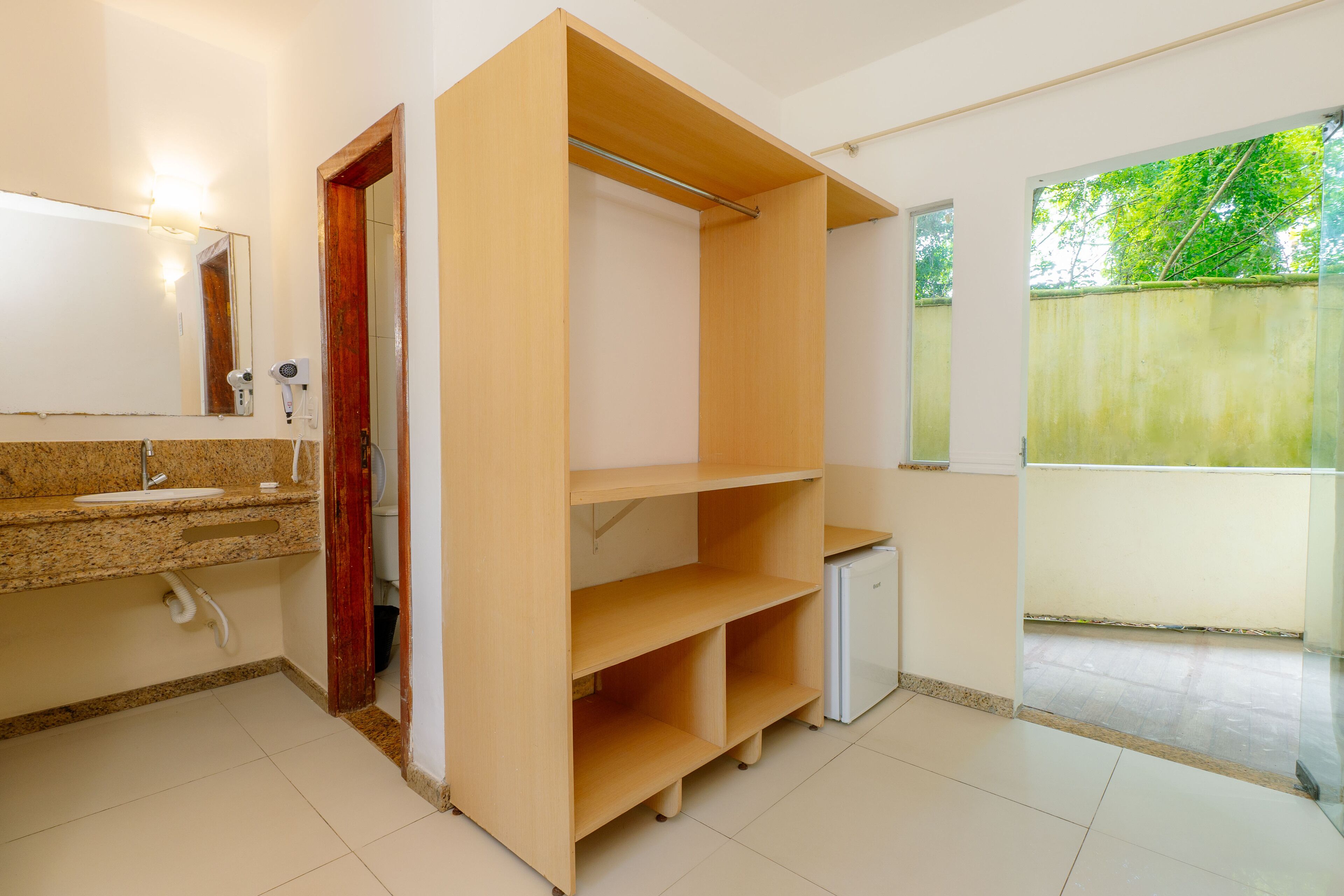 Un baño con encimera de granito, un espejo, un secador de pelo y una estantería de madera.