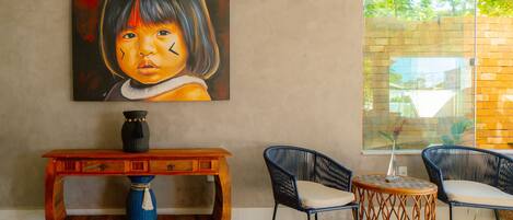 A room with a large painting, a wooden console table, two wicker chairs, and a small round table.