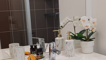 Une salle de bain avec un lavabo blanc, des distributeurs de savon en marbre et une orchidée en pot.