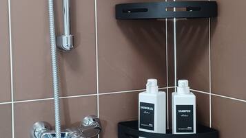 Ein Badezimmer mit Dusche, Duschbrausehandstück und zwei Flaschen Duschgel und Shampoo auf einem schwarzen Regal.