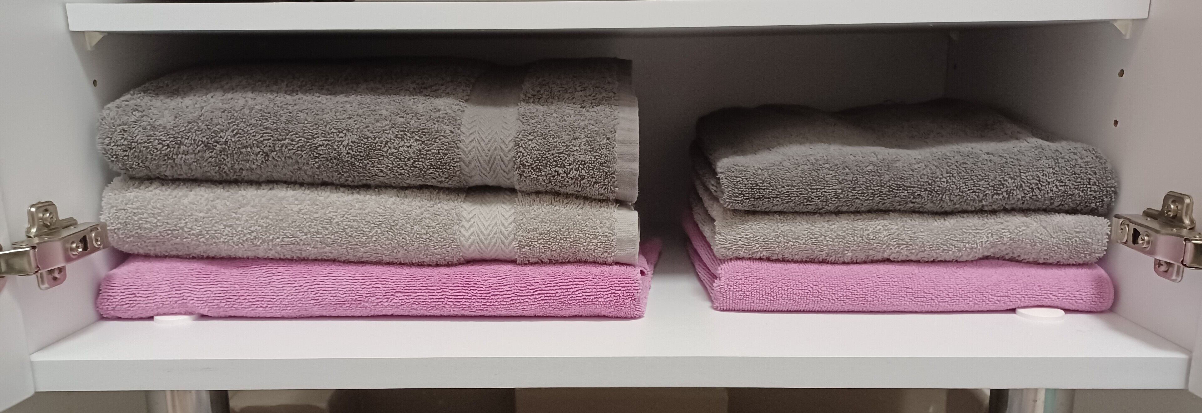 Un meuble de rangement doté de deux étagères, chacune contenant des serviettes pliées dans des tons de gris et de rose.