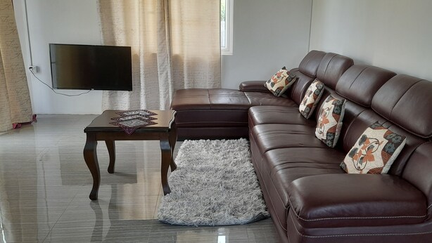 A living room with a brown leather sofa, a flat-screen TV mounted on the wall, a small wooden coffee table, and a fluffy white rug. - Cozy Appartment (Ebene City)