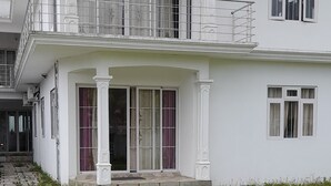 A two-story white building with a balcony, large windows, and a stone pathway leading to the entrance. - Cozy Appartment (Ebene City)
